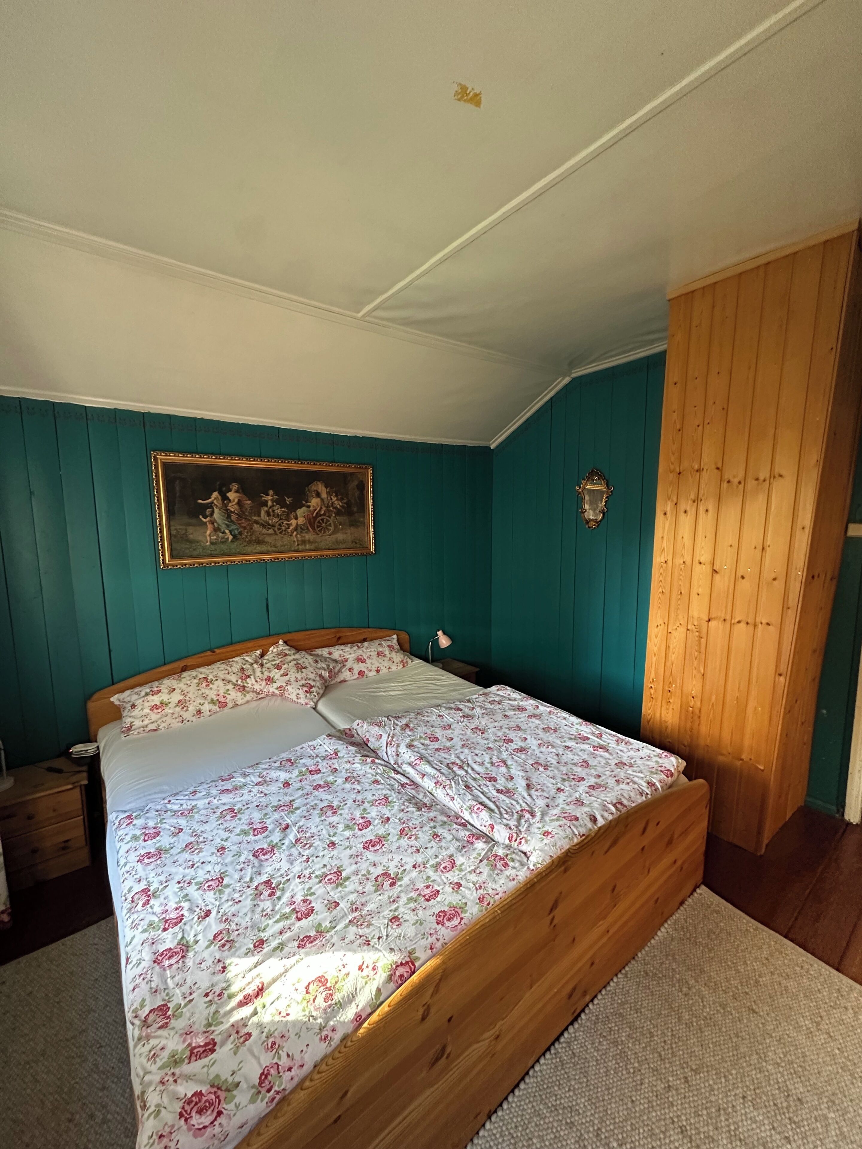 Ein Schlafzimmer mit einem hölzernen Bett, tealfarbenen Wänden, einem gerahmten Bild und einem Holzschrank.