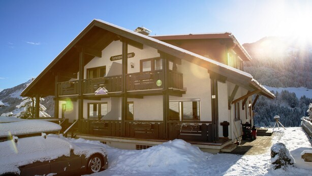 A two-story chalet with a balcony, a ski lift, and a snow-covered landscape.