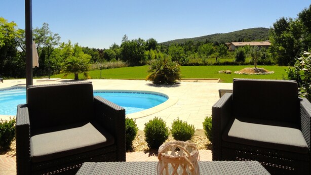 A poolside area with two wicker chairs and a table, surrounded by greenery and a view of a house in the background. - GARD - Near UZES - Villa standing 8 people - Quiet - Swimming pool - Petanque - View (Rousson)