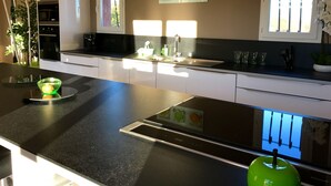 A modern kitchen with a black countertop, white cabinets, a built-in oven, and a window with a view of trees. - GARD - Near UZES - Villa standing 8 people - Quiet - Swimming pool - Petanque - View (Rousson)