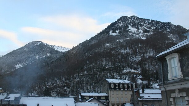 A mountain with snow-covered peaks and a town with buildings in the foreground.