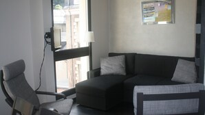 A modern room with a dark sofa, a grey armchair, and a small table. There is a window with a view of buildings outside.