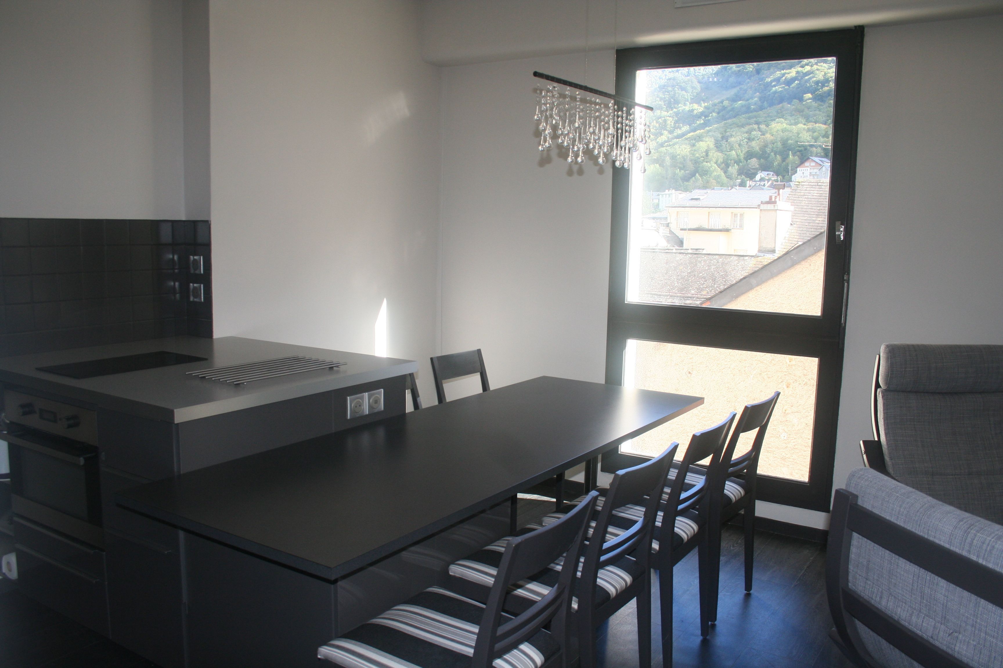 Une cuisine moderne dotée d’un grand îlot central, d’un coin repas avec des chaises et offrant une vue sur un paysage montagneux grâce à une grande fenêtre.