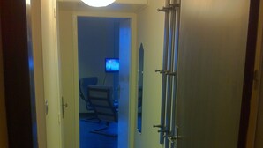 A hallway with a door on the right, a wall-mounted radiator, and a television in the background.