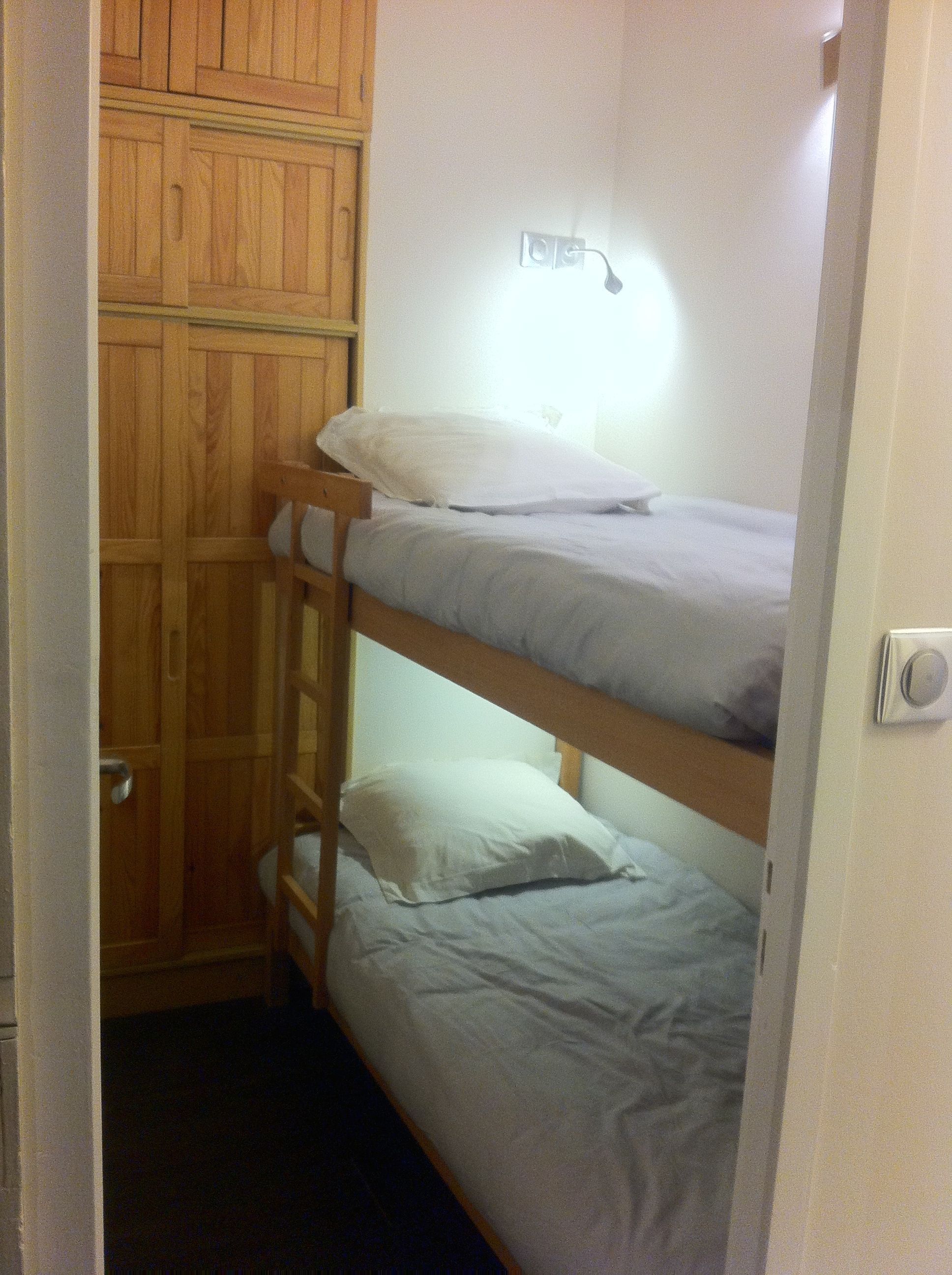 A bunk bed with a wooden wardrobe and a wall-mounted light fixture.