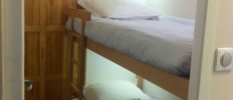 A bunk bed with a wooden wardrobe and a wall-mounted light fixture.