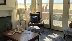 Une pièce avec une table en bois, une chaise, un lampadaire et une vue sur la plage, visible à travers de grandes portes coulissantes.