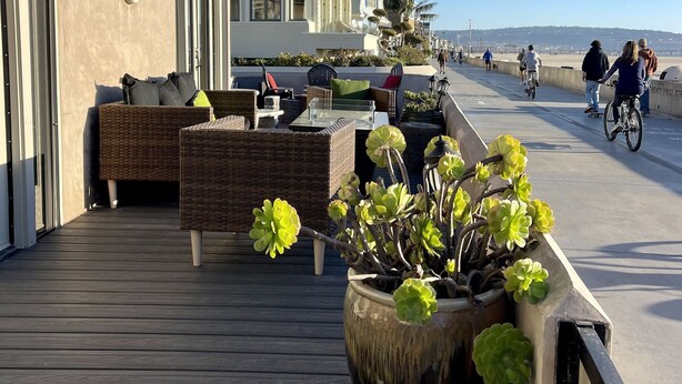 Une terrasse en bois, meublée de mobilier en osier, et un grand bac à fleurs contenant des plantes vertes.