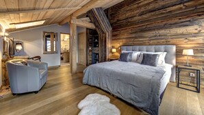 Een slaapkamer met een groot bed, een stoel, een houten plafond en een badkamer zichtbaar door een geopende deur.