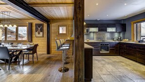 Een moderne keuken met donkere kastjes, een centraal eiland en een eethoek met een houten tafel en stoelen.