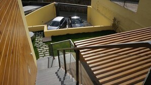 Un edificio moderno con fachada amarilla, una escalera de madera y un estacionamiento con dos coches.