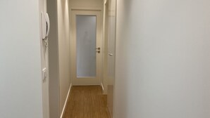 Un estrecho pasillo con suelo de madera y paredes blancas.