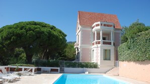 A pool area with a clear blue pool, white lounge chairs, and a building with a red-tiled roof. - Luxury  apartment  in an Art Nouveaux House Cavalaire Sur  Mer, near St Tropez (Cavalaire-Sur-Mer)