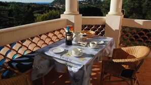 A terrace with a table set for two, a wicker chair, and a view of the landscape. - Luxury  apartment  in an Art Nouveaux House Cavalaire Sur  Mer, near St Tropez (Cavalaire-Sur-Mer)