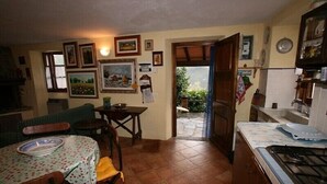 A cozy kitchen with a dining table, chairs, and a stove. There are framed pictures on the walls and a window with curtains. - DELICIOUS RUSTIC WITH PRIVATE GARDEN AND TERRACE A FEW KM. FROM THE SEA.  (Retignano)