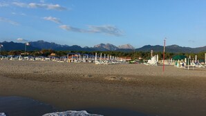 A beach with umbrellas and lounge chairs, a flag, and mountains in the background. - DELICIOUS RUSTIC WITH PRIVATE GARDEN AND TERRACE A FEW KM. FROM THE SEA.  (Retignano)