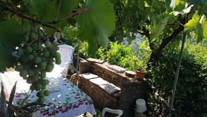 A rustic outdoor seating area with a stone bench, a table with a floral tablecloth, and a view of a vineyard. - DELICIOUS RUSTIC WITH PRIVATE GARDEN AND TERRACE A FEW KM. FROM THE SEA.  (Retignano)