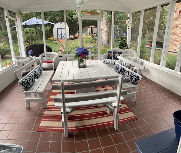 A covered patio with a wooden table and benches, surrounded by a garden view.