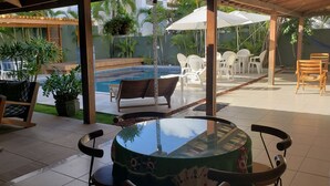 Un espacio al aire libre techado con piscina, sillas y mesas.