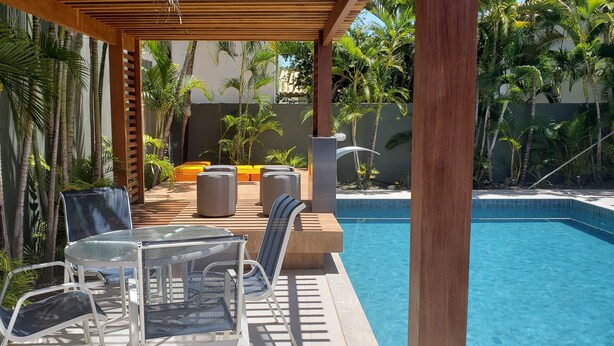 Un área junto a la piscina con sillones, una mesa y una pérgola.