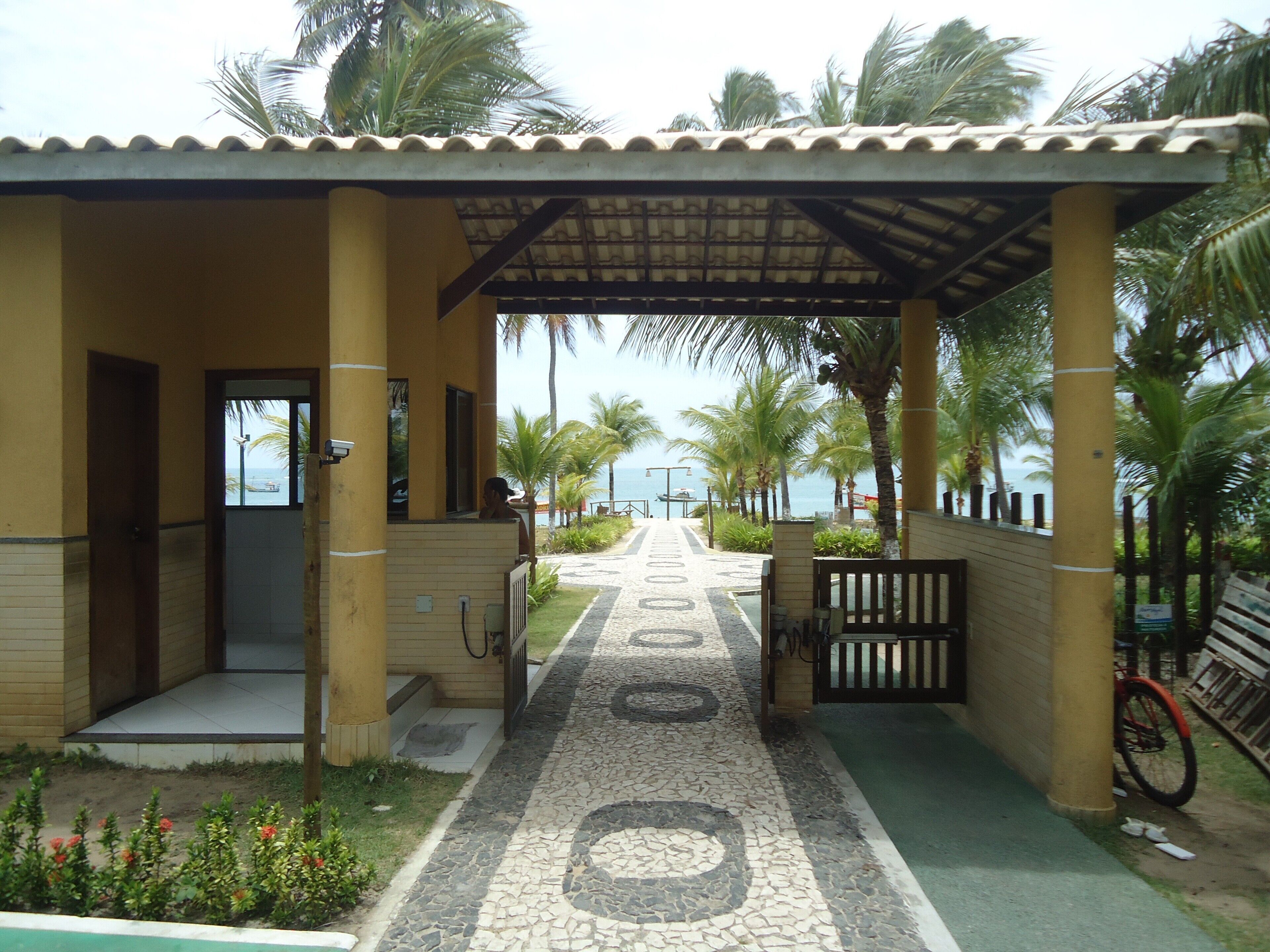 A covered walkway leading to a building with a tiled floor and palm trees.