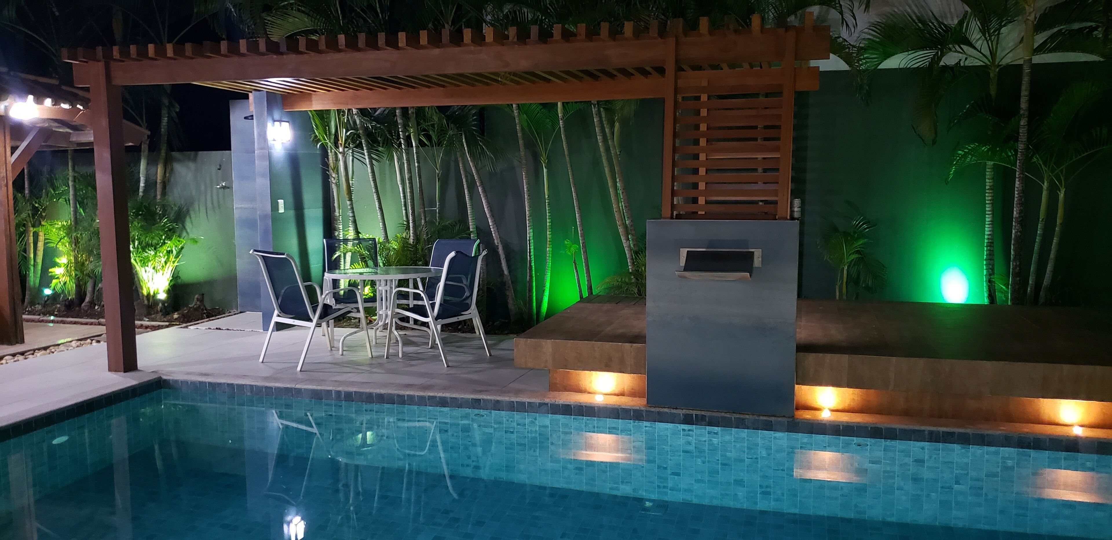 Et poolområde med pergola, siddepladser og et lille bord.