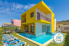 A two-story yellow building with a swimming pool, a covered patio, and a checkered flag indicating cleanliness. - V4 Villa with private pool, garden and sea views (Albufeira)