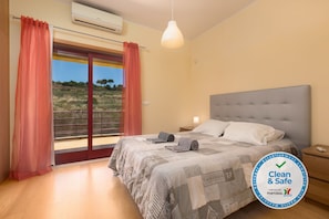 A bedroom with a large bed, a window with curtains, a hanging light, and a logo on the wall. - V4 Villa with private pool, garden and sea views (Albufeira)