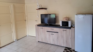 A compact kitchen with a microwave, a small refrigerator, a television on a wooden cabinet, and a door leading to a garage.