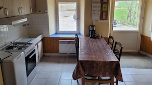 A kitchen with a stove, oven, and a dining table with chairs. There are windows and a view of the outside.