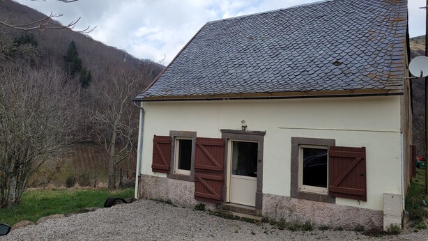 A small house with a sloped roof, wooden shutters, and a stone foundation.