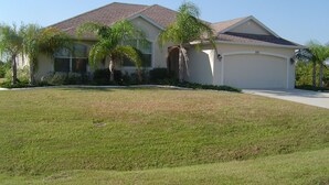 A single-story house with a sloped roof, a garage, and a well-maintained lawn with palm trees. - Baytree Vacation Villa-- (Rotonda Lakes)