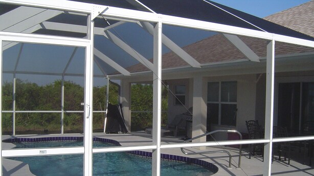 A covered outdoor swimming pool with a glass enclosure, a patio area with chairs, and a view of the surrounding landscape. - Baytree Vacation Villa-- (Rotonda Lakes)