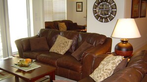 A living room with a brown leather sofa, a wooden coffee table, and a wall clock. - Baytree Vacation Villa-- (Rotonda Lakes)