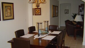 A dining area with a wooden table, chairs, and a chandelier. There are framed pictures on the walls and a lamp in the background. - Baytree Vacation Villa-- (Rotonda Lakes)