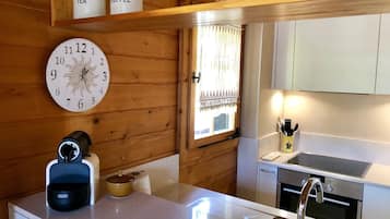 Une cuisine avec des murs en bois, une horloge ronde, une étagère pour les boîtes à café et à thé, une machine à café et un évier doté d'un robinet moderne.