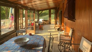 A covered patio area with a table and chairs, a wooden ceiling, and a view of the outdoors.