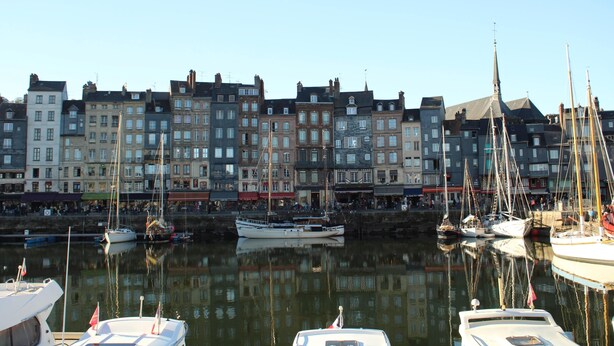 A marina with several boats docked, surrounded by multi-story buildings with varied architectural styles.