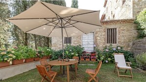 A patio with a round wooden table and chairs, a large beige umbrella, and flower planters. - Apartment in Country Villa and  SPA (Vicchio (Firenze))