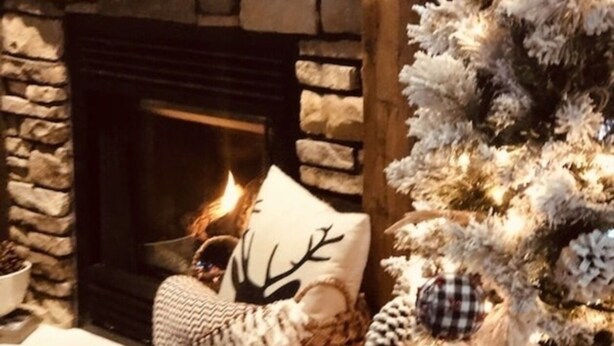 A stone fireplace with a lit fire, a decorated Christmas tree, and a checkered cushion on the mantel. - Peaceful Quiet Getaway in Amish Country!10 min. to Berlin & Walnutcreek. #hotub (Dundee)