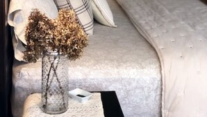 A bedroom with a bed, pillows, a vase with dried flowers, a lamp, and a door with a barn-style design. - Peaceful Quiet Getaway in Amish Country!10 min. to Berlin & Walnutcreek. #hotub (Dundee)