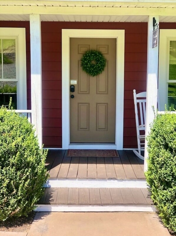 Puerta principal con corona decorativa, buzón y una silla blanca en el exterior.