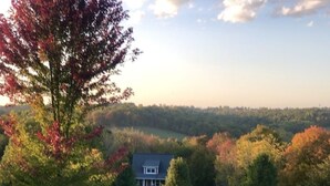 A house surrounded by trees with autumn foliage, a fenced yard, and a hilly landscape in the background. - Peaceful Quiet Getaway in Amish Country!10 min. to Berlin & Walnutcreek. #hotub (Dundee)