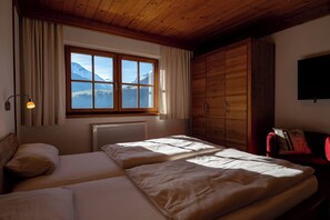 A room with two beds, a window with a mountain view, a radiator, and a television on the wall.