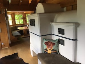 L’intérieur d’un chalet accueillant, avec un plafond en bois, un banc agrémenté d’un coussin orné d’une vache, et une fenêtre donnant sur un paysage verdoyant.