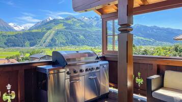 Una parrilla de acero inoxidable sobre una terraza de madera, con vista a montañas y un cielo despejado.