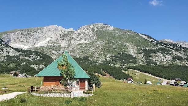 Un rifugio di montagna con tetto verde, circondato da un prato e una recinzione in legno.