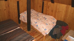 Una stanza accogliente e piccola con un letto singolo, pareti in legno e un soffitto spiovente.