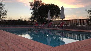 Una piscina con sillas de descanso y sombrillas, rodeada por una valla de madera y árboles.