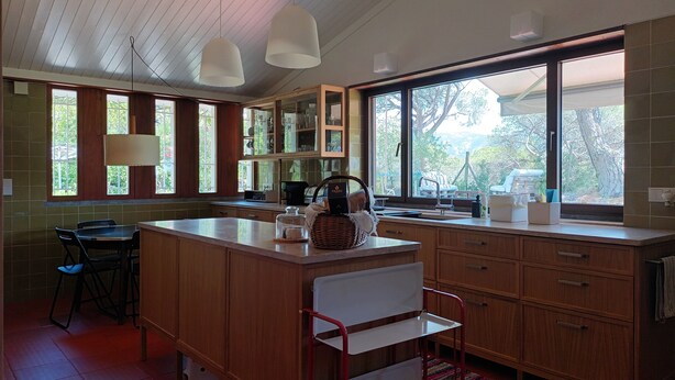Una cocina moderna con armarios de madera, una isla central y grandes ventanales con vistas al exterior.